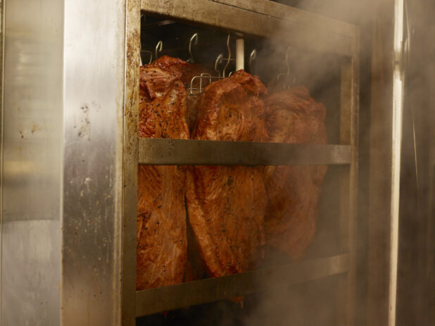 Pastrami hanging in a smoker in a restaurant