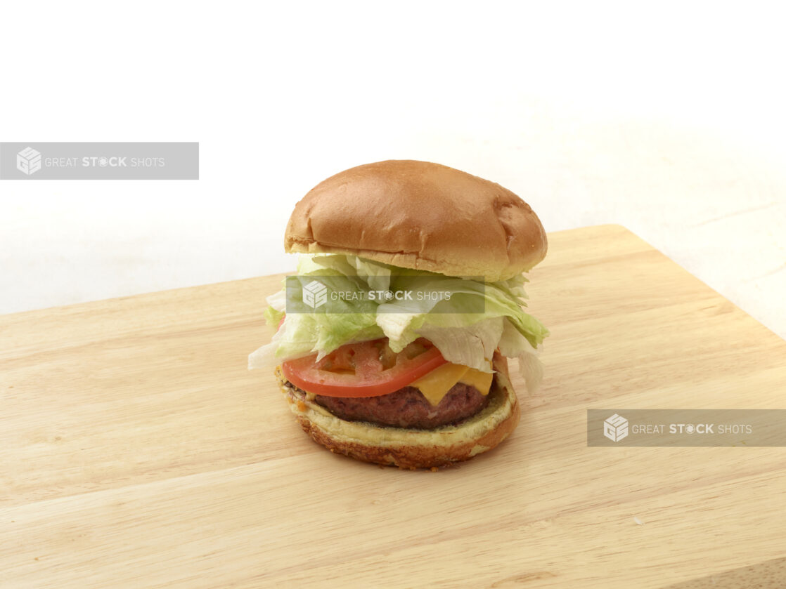 Hamburger with cheese, lettuce and tomato on a bun sitting on a wooden cutting board