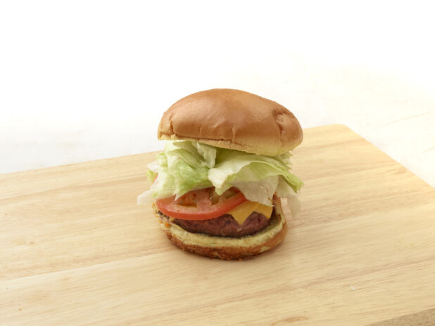 Hamburger with cheese, lettuce and tomato on a bun sitting on a wooden cutting board