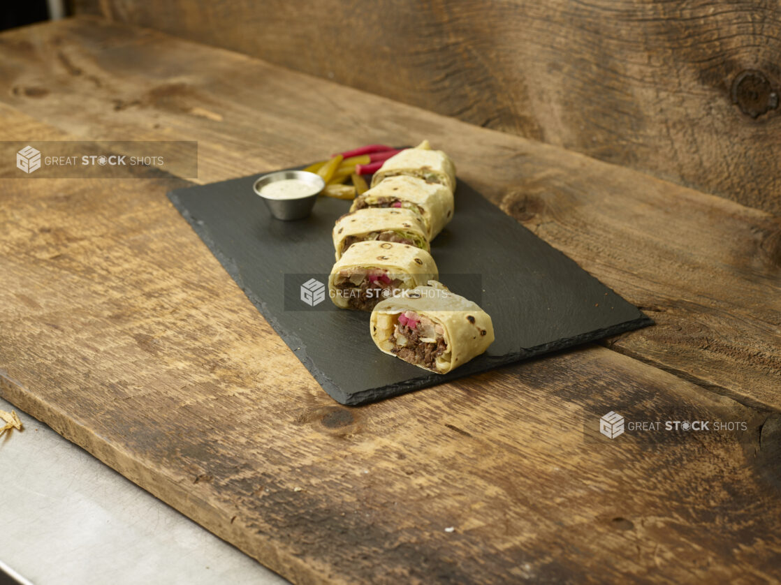 Beef shawarma cut in pieces on a slate platter with pickles, pickled turnip and dip