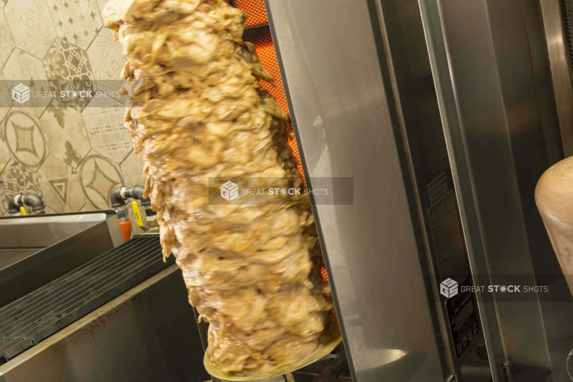 Close up shot of chicken shawarma on vertical broiler, beside other kitchen equipment