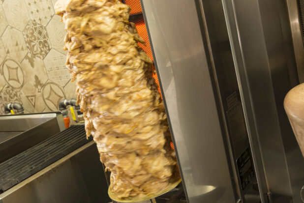 Close up shot of chicken shawarma on vertical broiler, beside other kitchen equipment