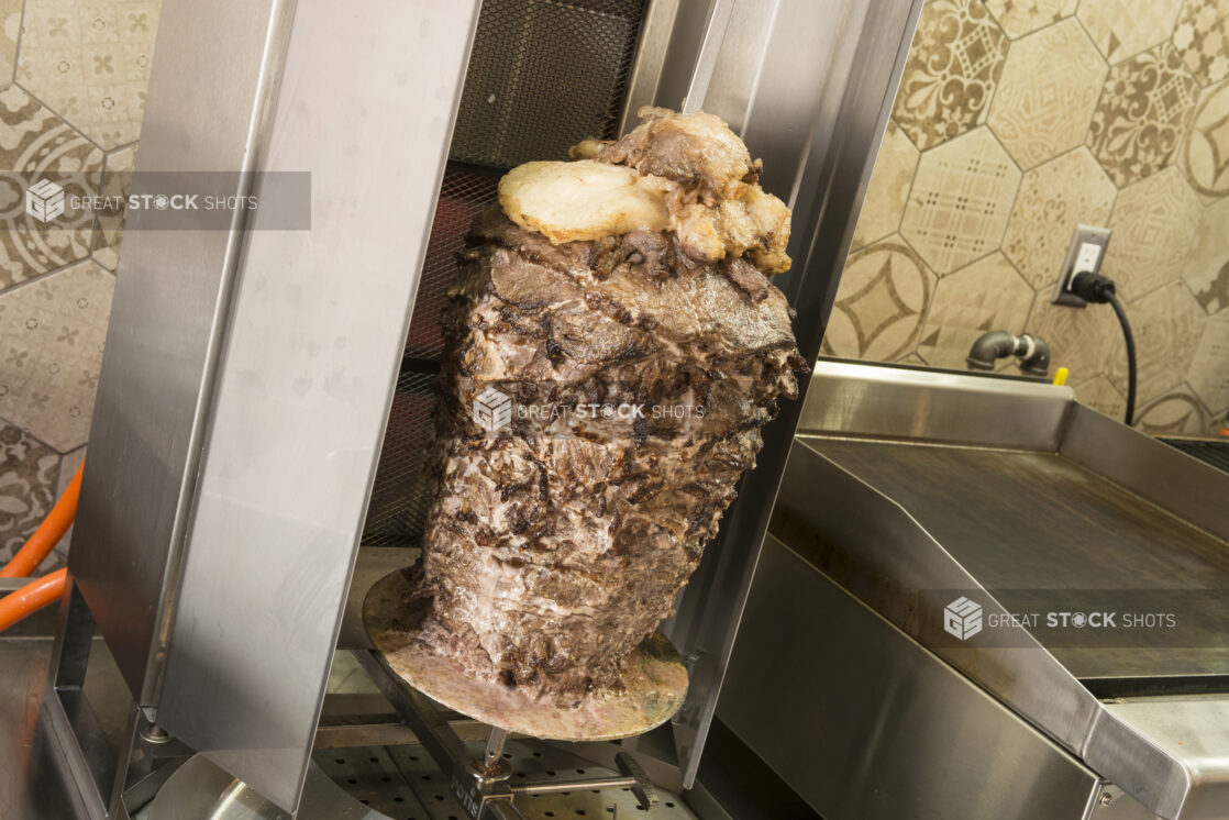 Vertical broiler with meat shawarma beside a flat top, shot on an angle