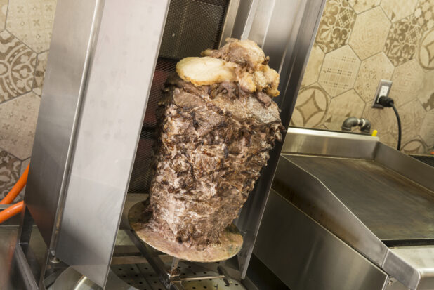 Vertical broiler with meat shawarma beside a flat top, shot on an angle