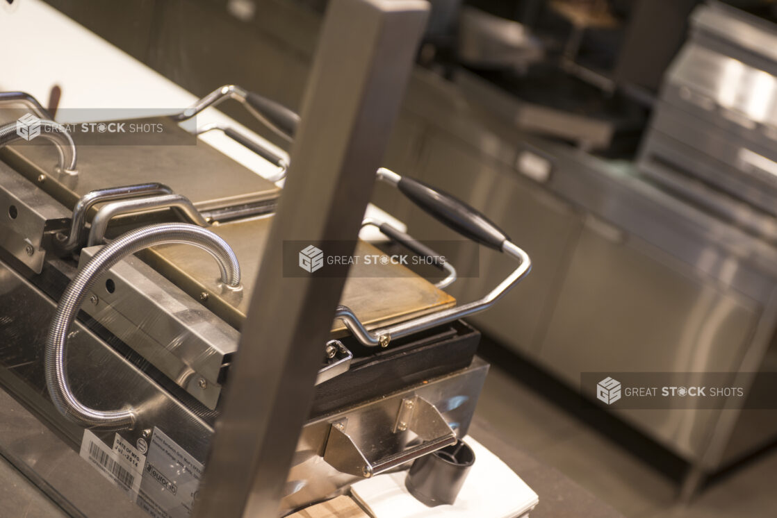 Off centre side view of 2 panini presses and restaurant kitchen