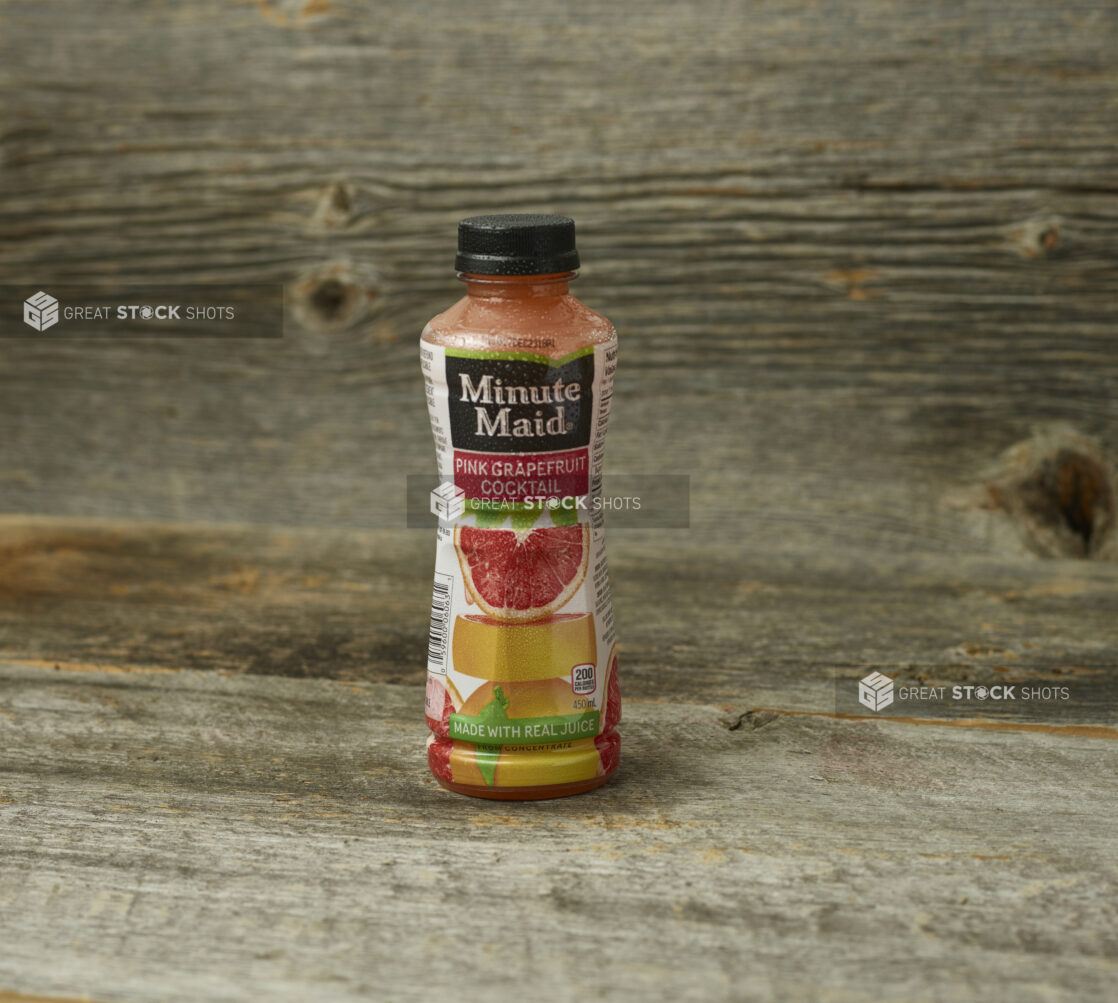 Minute Maid pink grapefruit cocktail in a plastic bottle on an aged wooden table and aged wooden background with a straight on view