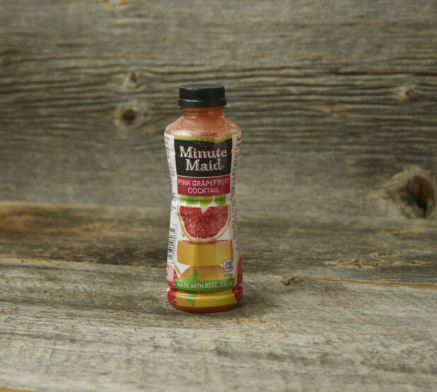 Minute Maid pink grapefruit cocktail in a plastic bottle on an aged wooden table and aged wooden background with a straight on view