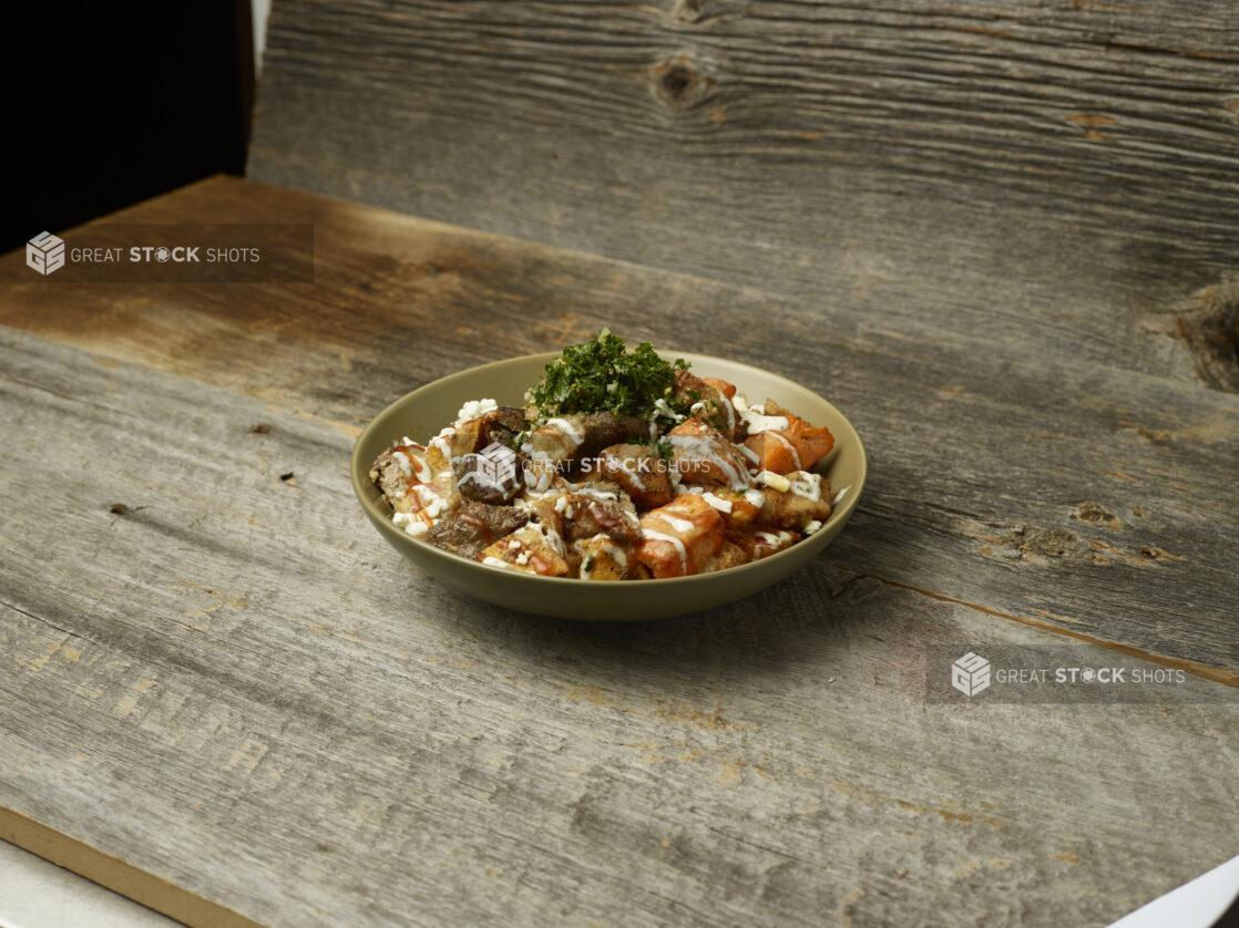 Meat shawarma potato bowl with parsley on top on an aged wooden table and aged wooden background