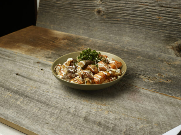 Meat shawarma potato bowl with parsley on top on an aged wooden table and aged wooden background