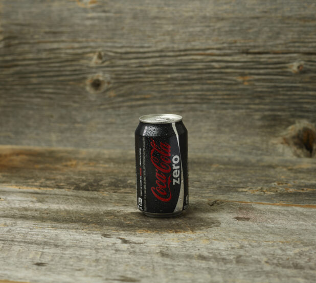 Coke Zero can on a wooden table with a wooden background and a straight on view