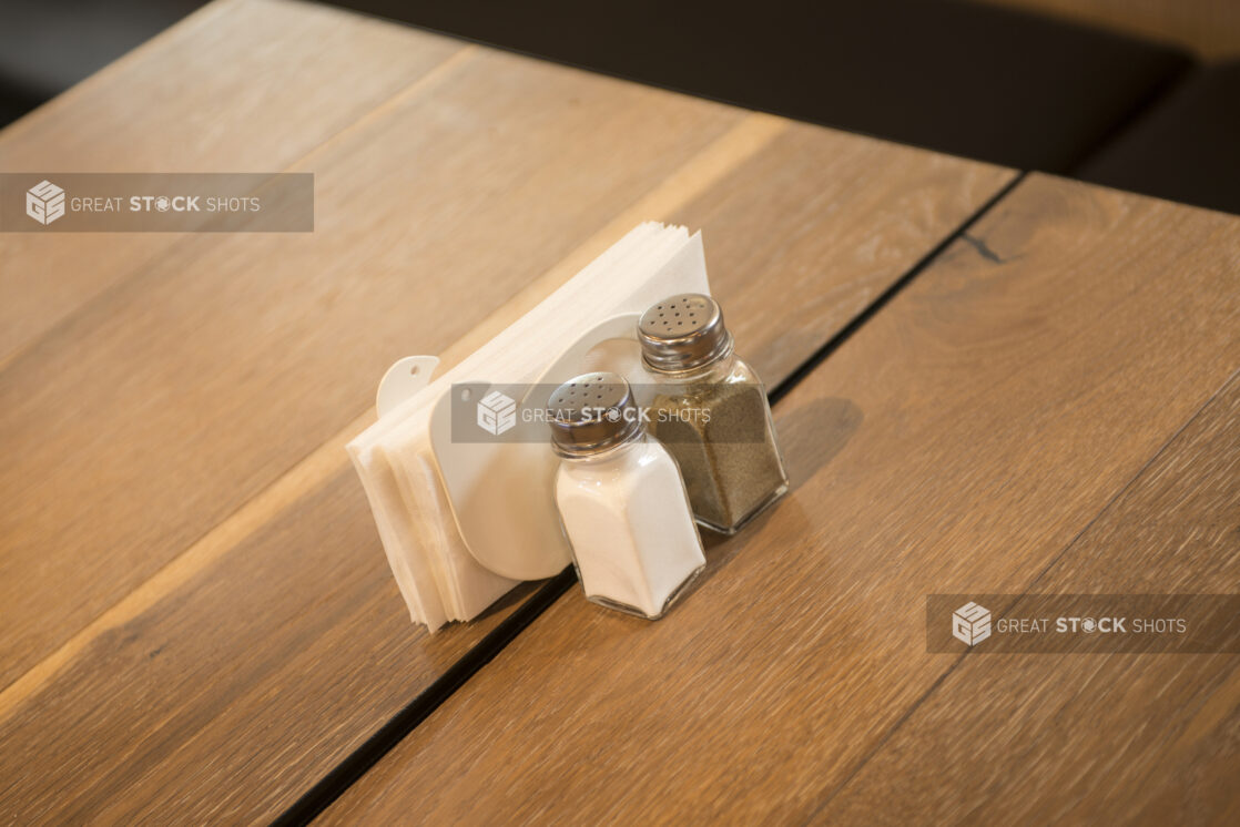 Salt and pepper shaker and napkin holder on a wooden restaurant table