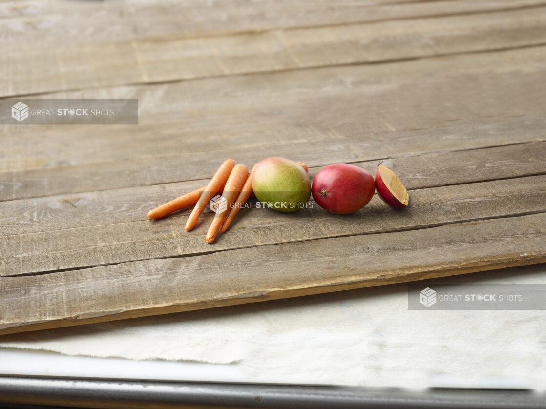 Whole carrots and mangoes on wooden planks