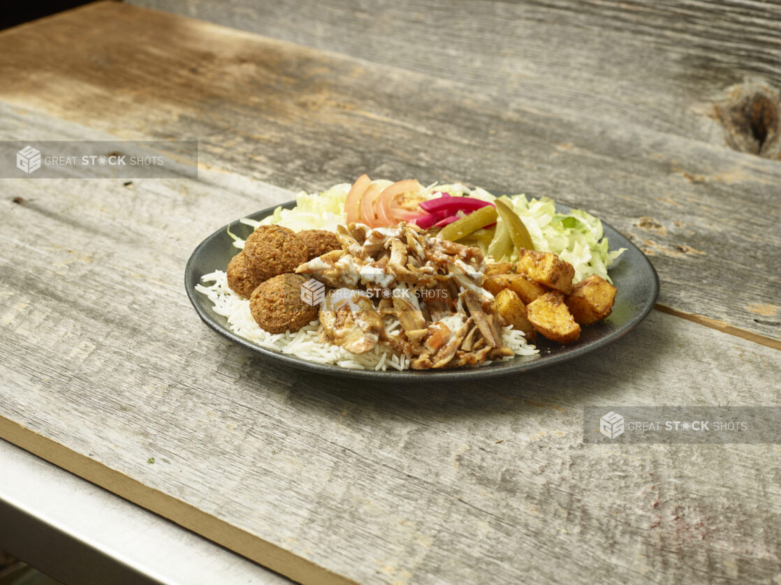 Chicken  shawarma & falafel dinner on a round plate on a wooden table with a wooden background