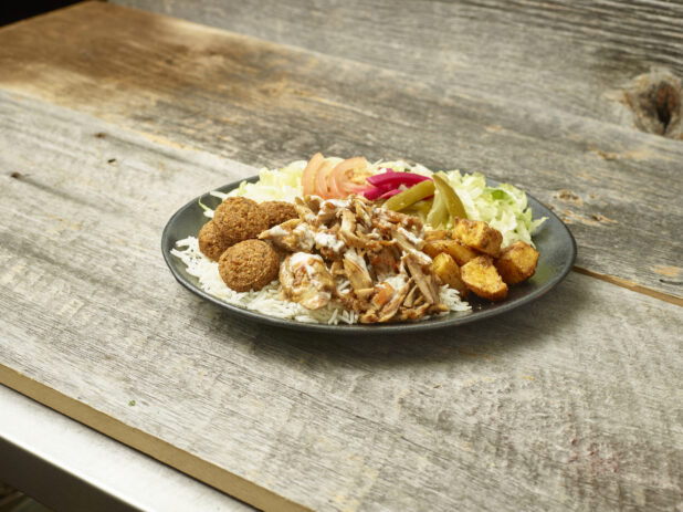 Chicken  shawarma & falafel dinner on a round plate on a wooden table with a wooden background