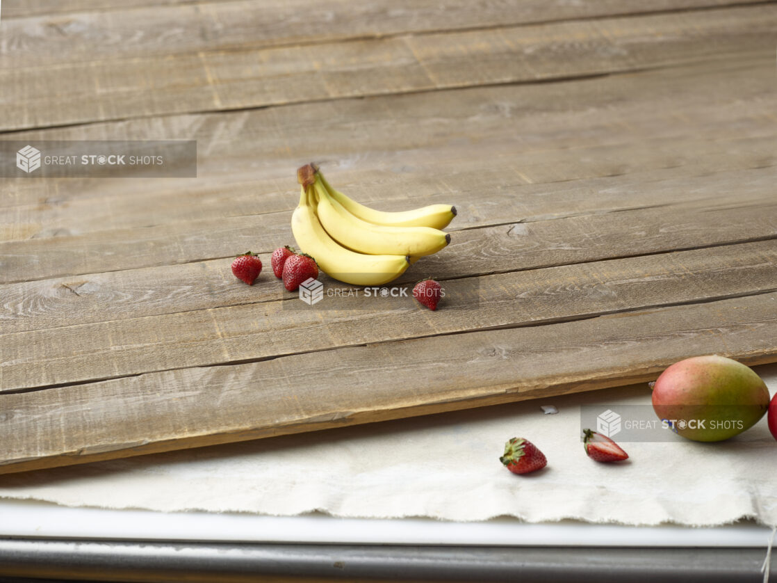 Whole bananas, strawberries and mango on wooden planks and muslin