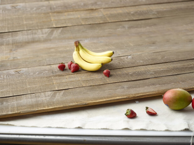 Whole bananas, strawberries and mango on wooden planks and muslin