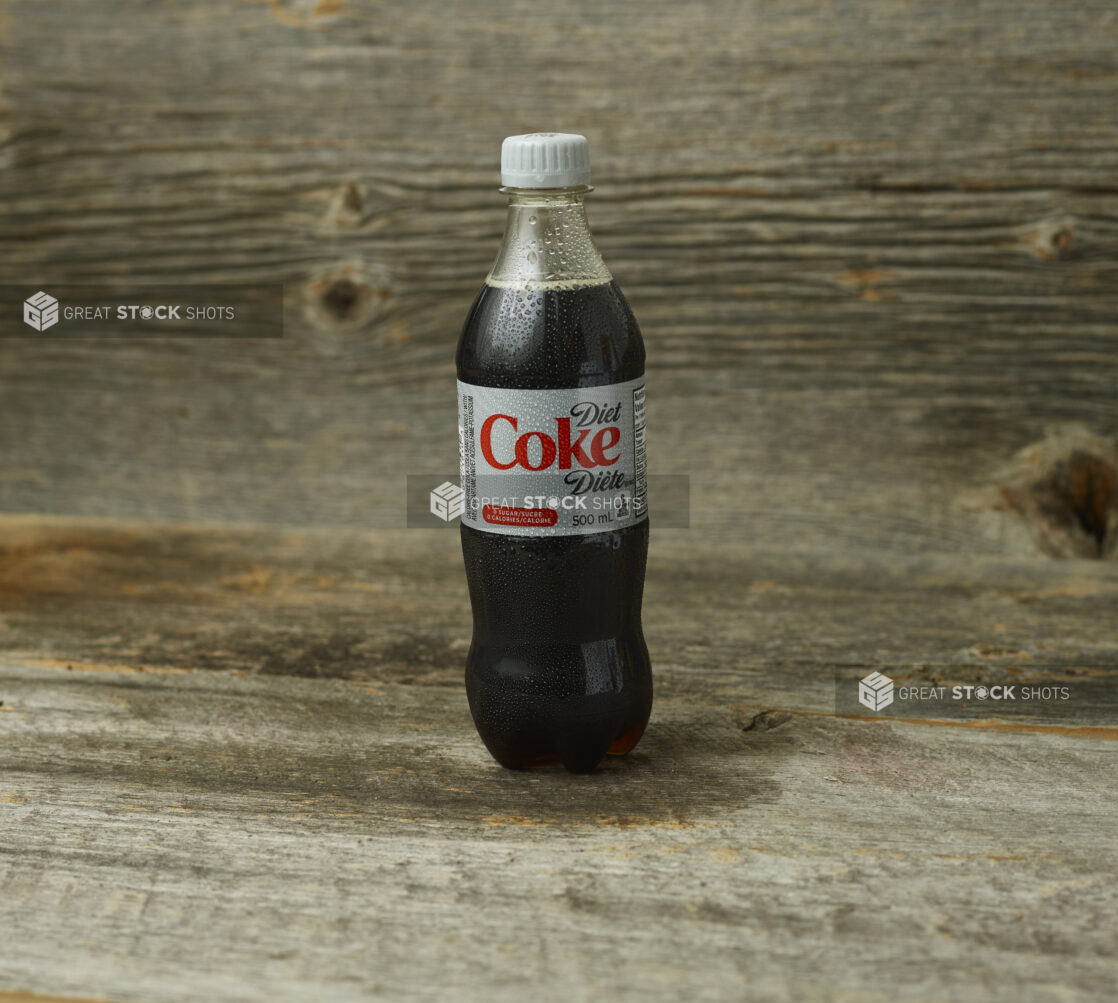 Diet Coke in a plastic bottle on a wooden table with a wooden background and a straight on view