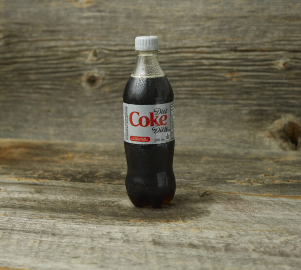 Diet Coke in a plastic bottle on a wooden table with a wooden background and a straight on view