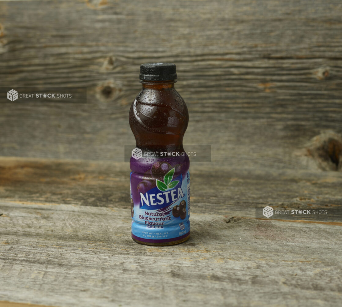 Nestea blackcurrant iced tea in a plastic bottle on a wooden table with a wooden background and a straight on view