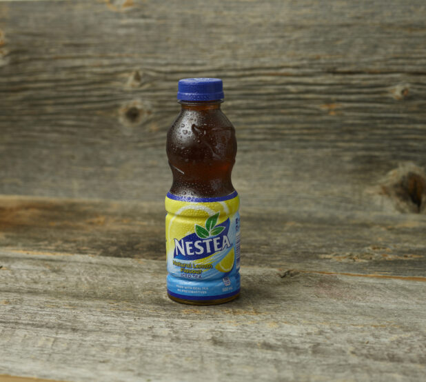 Nestea Natural Lemon iced tea in a plastic bottle on a wooden table with a wooden background and straight on view