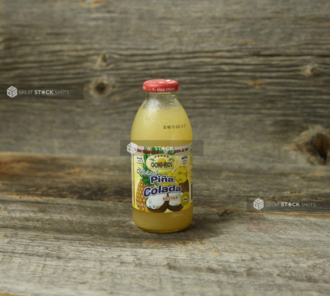 Pina Colada tropical juice in a glass bottle on a wooden table with wooden background and staright on view