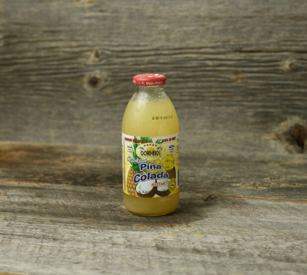 Pina Colada tropical juice in a glass bottle on a wooden table with wooden background and staright on view