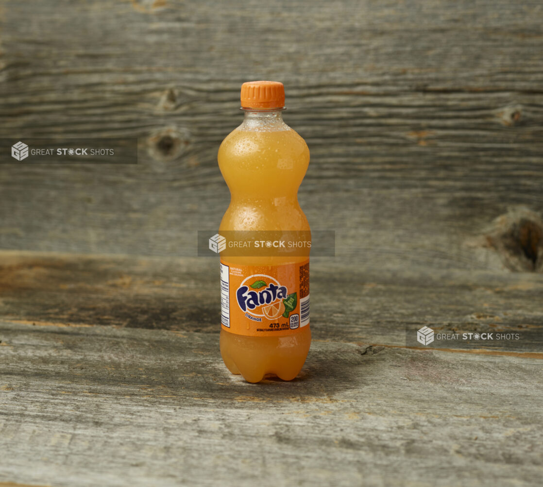 Fanta orange soda in a plastic bottle on a wooden table with a wooden background and straight on view