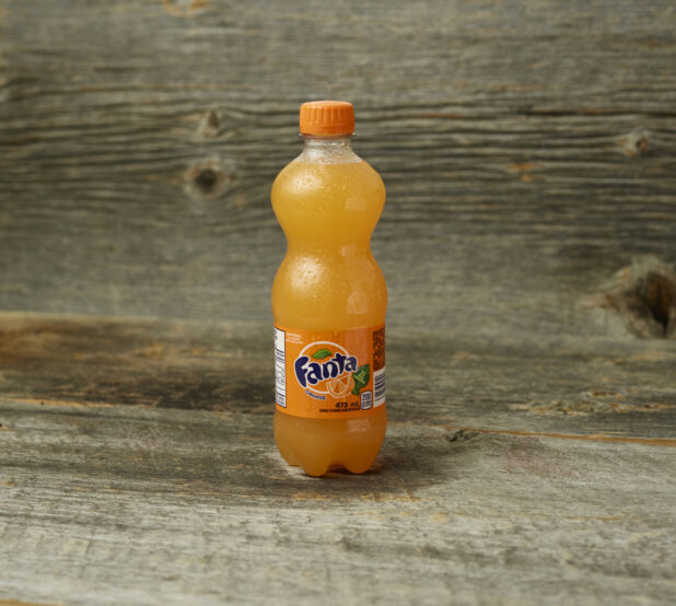 Fanta orange soda in a plastic bottle on a wooden table with a wooden background and straight on view