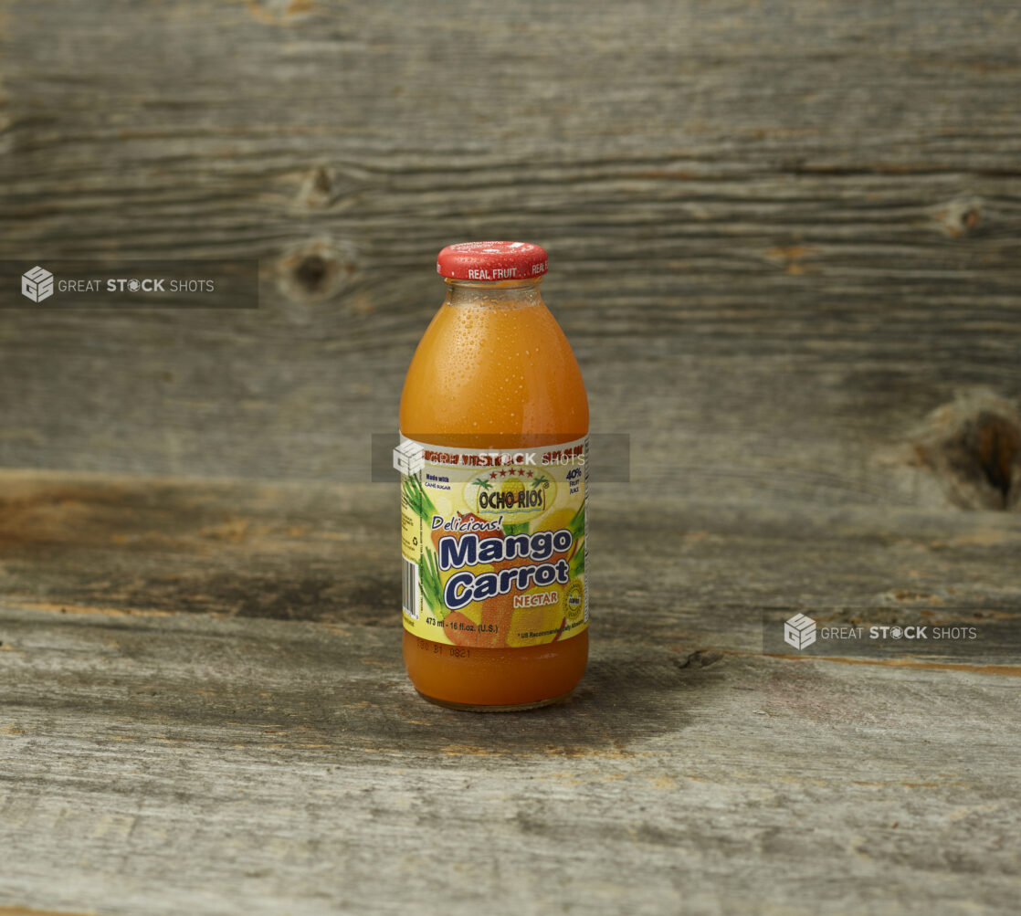 Tropical mango carrot juice in a glass bottle on a wooden table with wooden background and straight on view