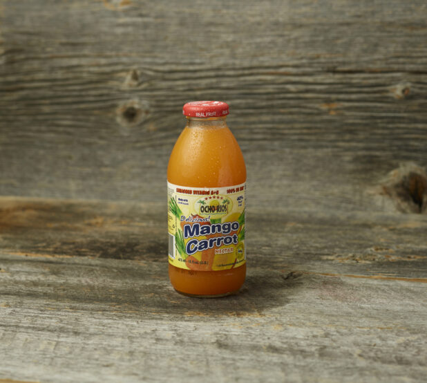 Tropical mango carrot juice in a glass bottle on a wooden table with wooden background and straight on view