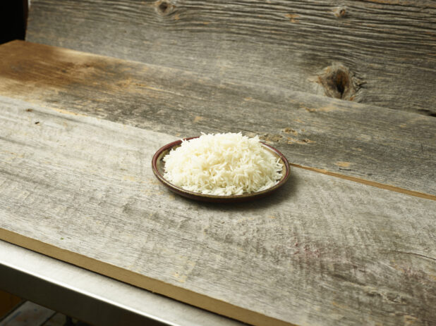 Cooked rice on a plate on a wooden background on a slight bias, rustic wood background