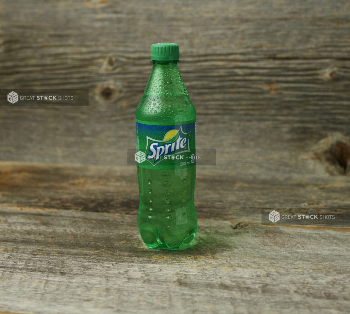 Sprite in a plastic bottle on a wooden table with a wooden background and a  straight on view