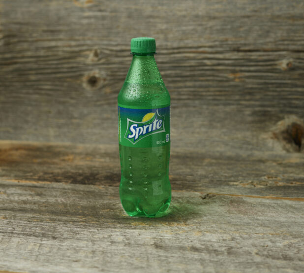 Sprite in a plastic bottle on a wooden table with a wooden background and a  straight on view