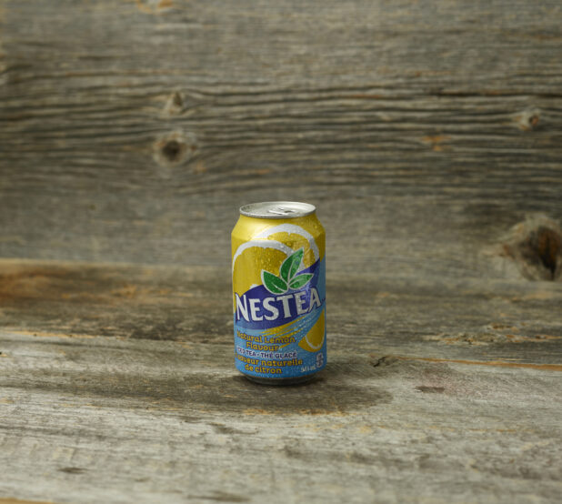 Nestea iced tea in a can on a wooden table with a wooden background and straight on view
