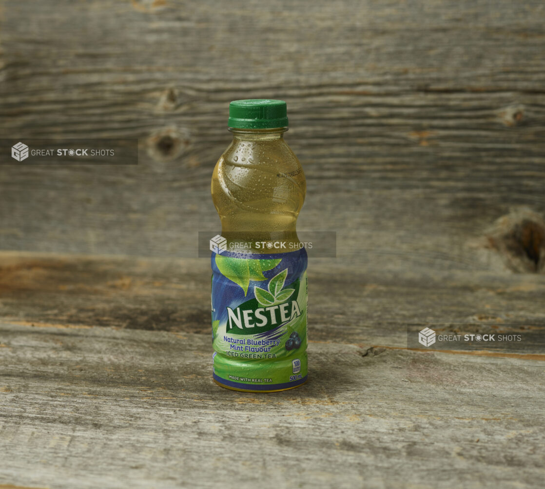 Nestea Blueberry Mint iced tea in a plastic bottle on a wooden table with a wooden background and straight on view