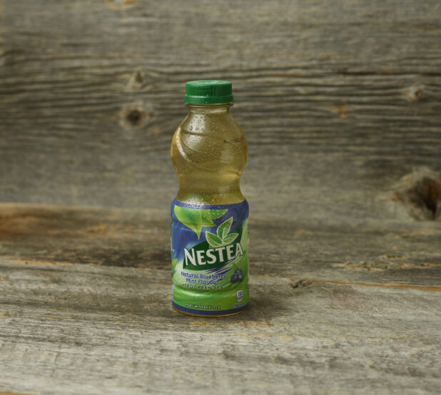 Nestea Blueberry Mint iced tea in a plastic bottle on a wooden table with a wooden background and straight on view