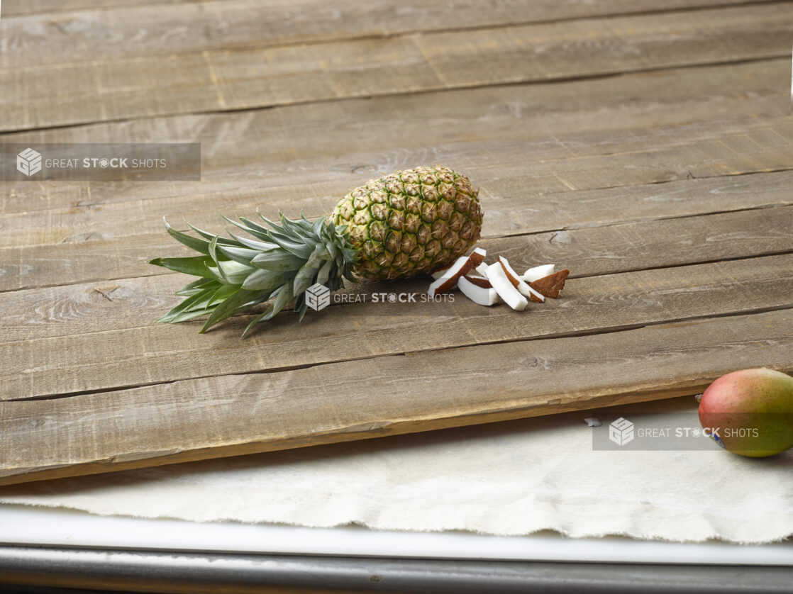 Whole pineapple with a whole mango and sliced coconut on a wooden table