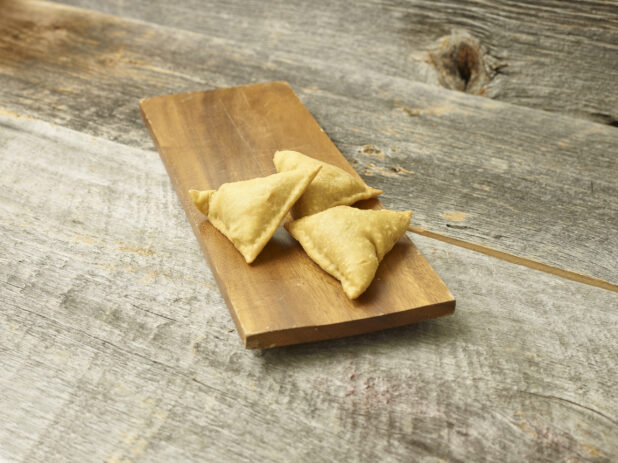 Samosa appetizer on a wooden platter on a wooden background