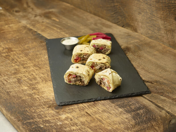 Shawarma bites on a slate platter with pickles, pickled turnip & dip on a wooden background slightly angled