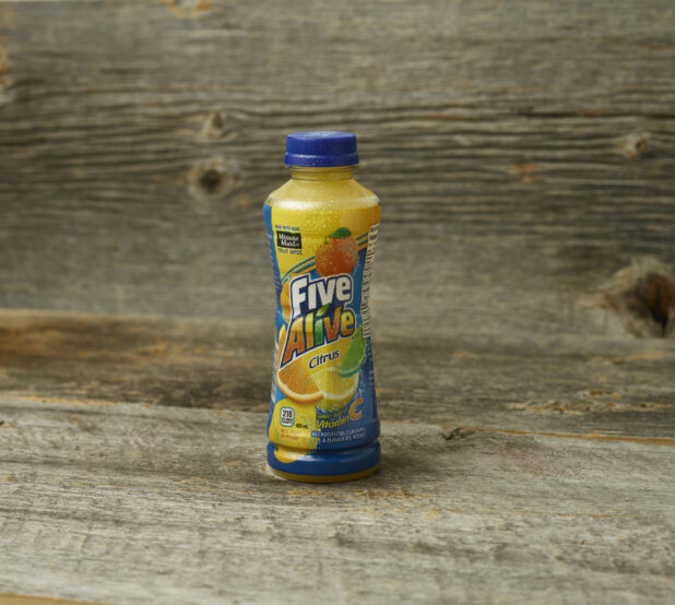 Five Alive juice in a plastic bottle on a wooden table with a wooden background and a straight on view