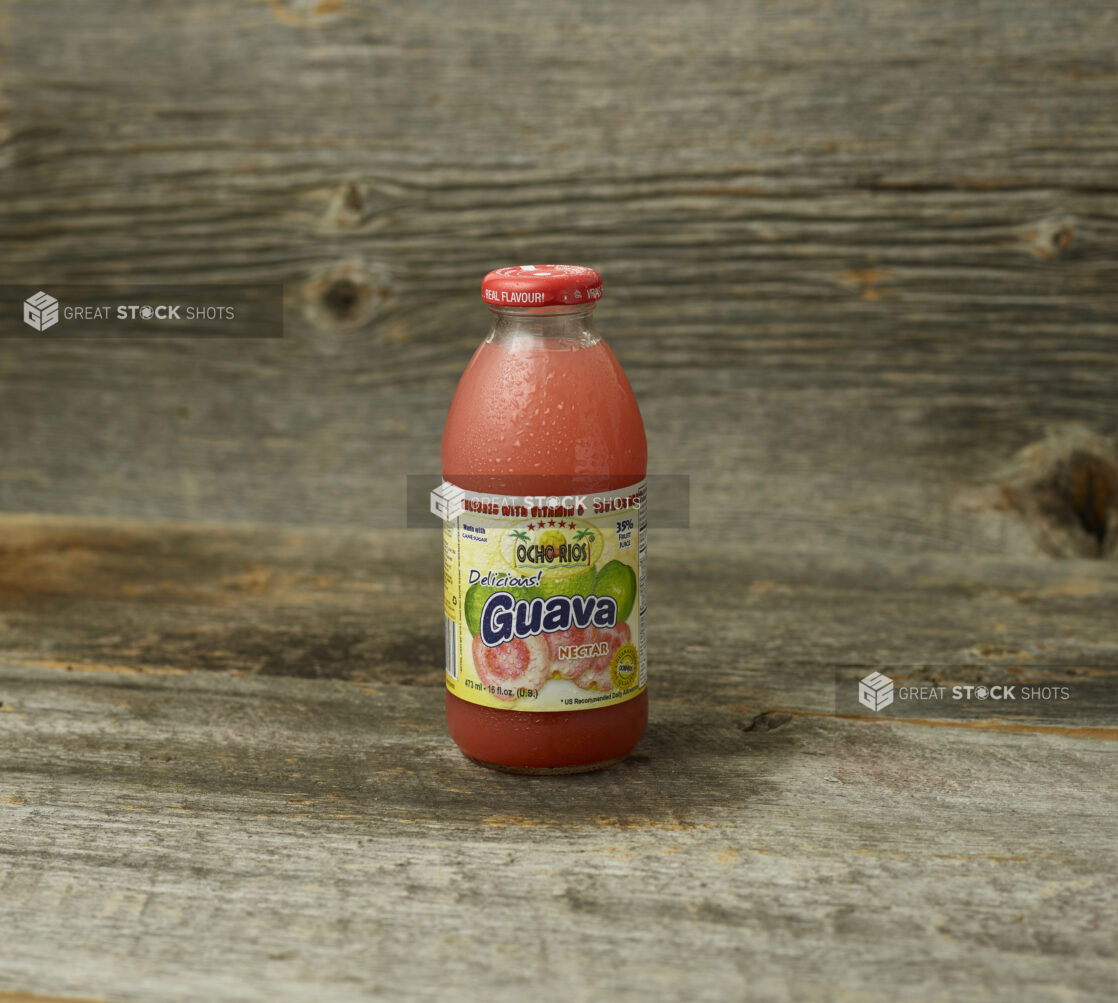 Guava juice in a bottle on a wooden table with a wooden background and a straight on view