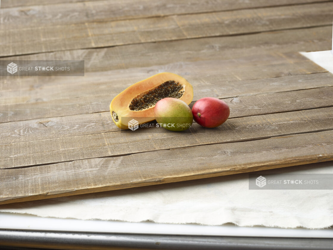 Half a papaya and 2 mangoes on wooden planks with an elevated straight on view