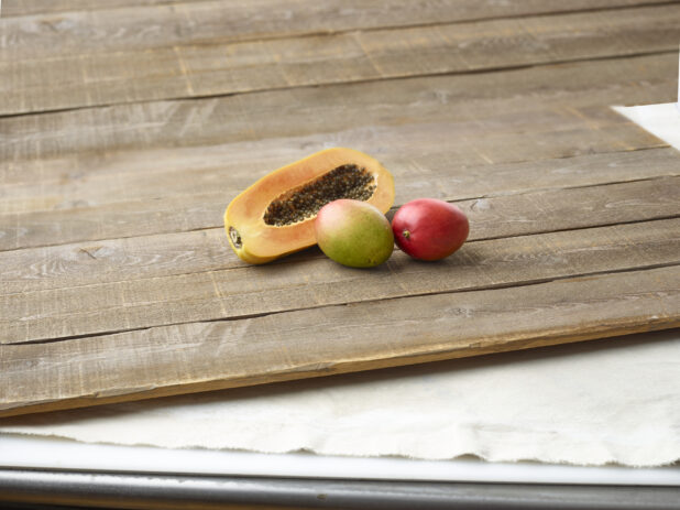 Half a papaya and 2 mangoes on wooden planks with an elevated straight on view