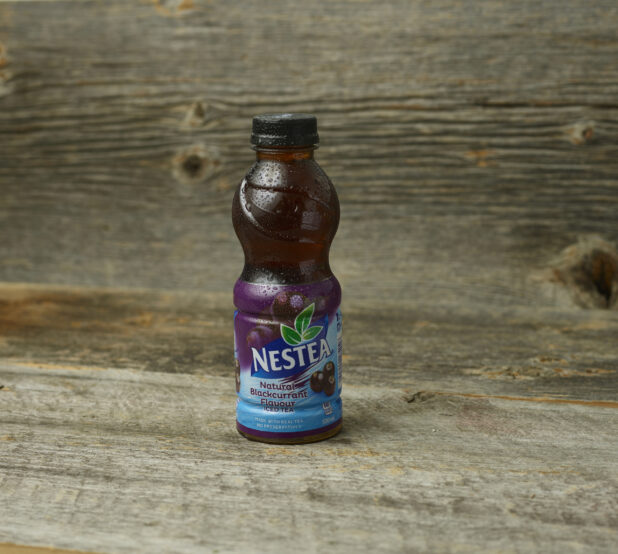 Nestea blackcurrant iced tea in a plastic bottle on a wooden table with a wooden background and a straight on view