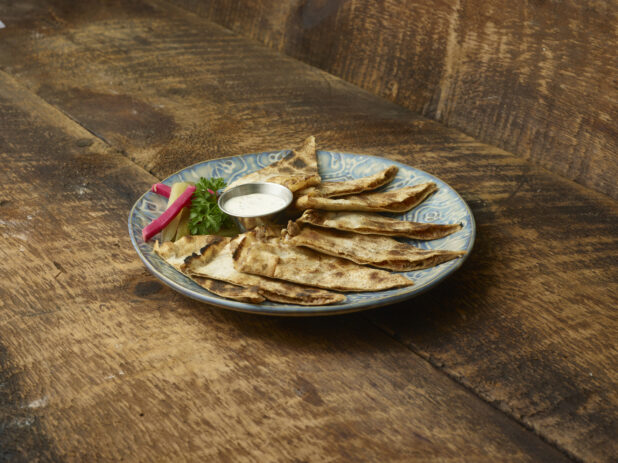 Sliced lahmajeen/middle eastern pizza on a decorative plate on a wooden table with a wooden background at a 45 degree angle