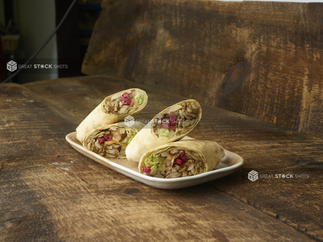 2 halved shawarma wraps on a white platter on a wooden table and background