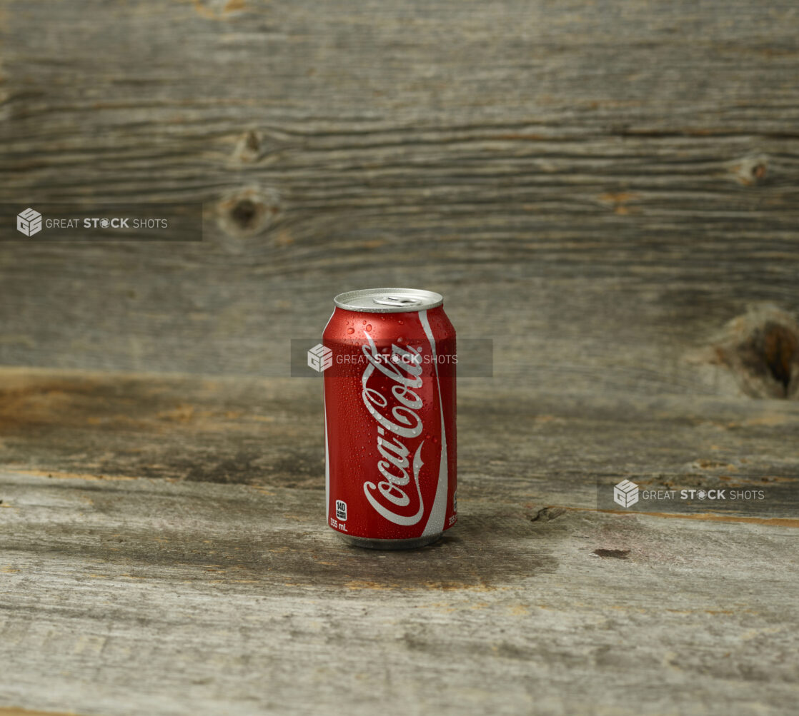 Straight on view of Coke can on a wooden table with a wooden background