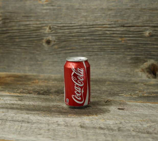 Straight on view of Coke can on a wooden table with a wooden background