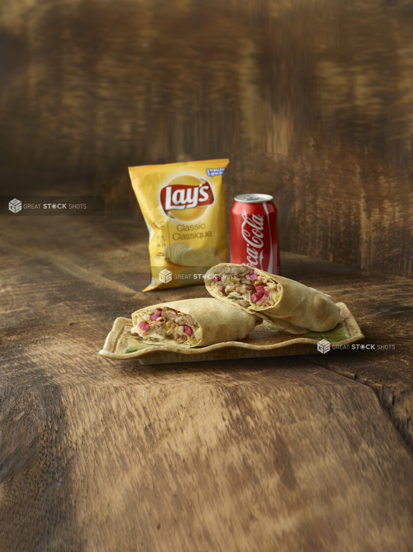 Shawarma wrap cut in half on a platter with coke and lays potato chips in background on a wooden background