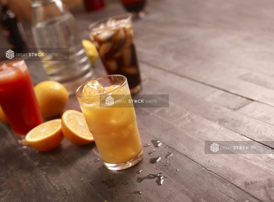 Beverages, orange juice, tomato juice and cola with sliced oranges and a carafe of water on a dark wooden background